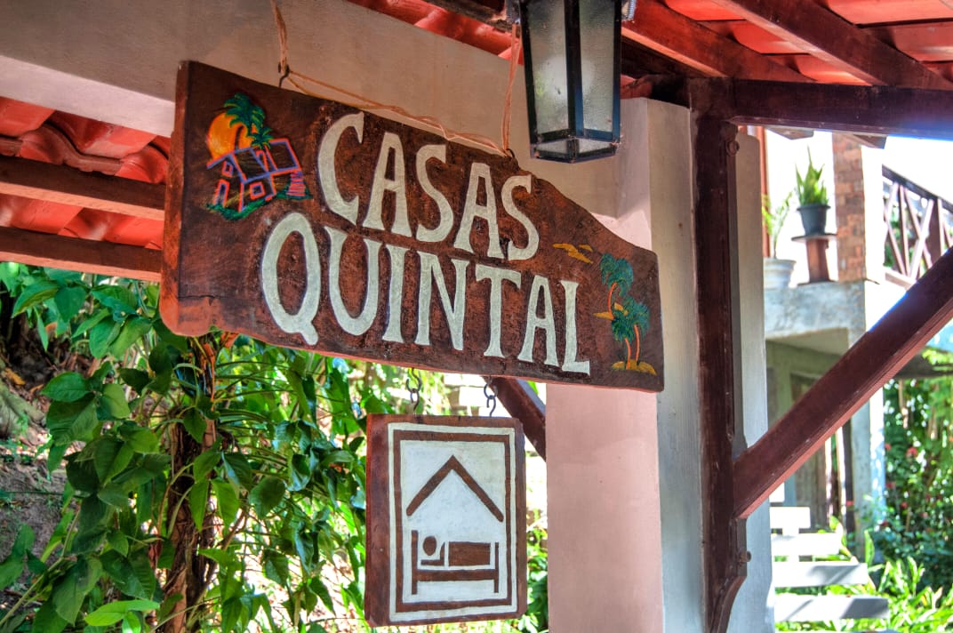 Placa artesanal de madeira das Casas Quintal entre a vegetação tropical